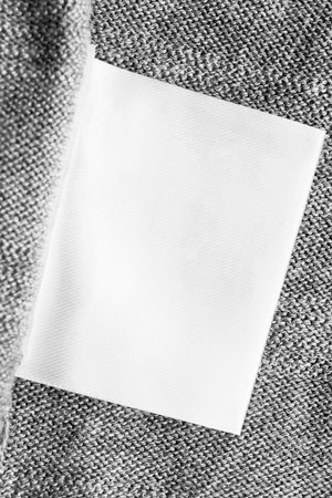 White blank clothes label on gray knitted cloth as a background closeup