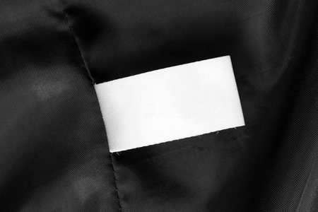 Blank white clothes label on black silk closeup as a background