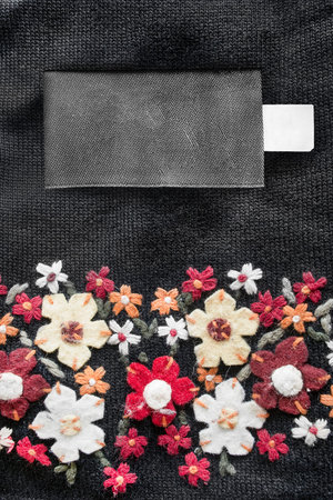 Blank clothes label on black knitwear background with felt colorful flowers