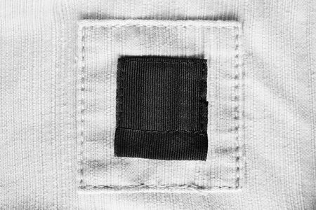 Blank black clothes label on white textile background closeup