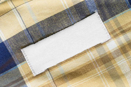 Blank white clothes label on yellow and blue tartan background