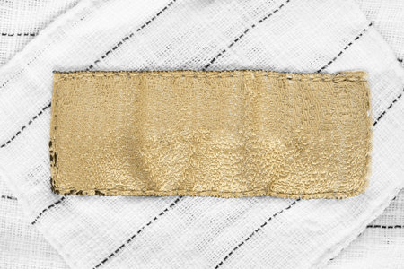 Blank golden clothes label on striped white textile background closeupの写真素材