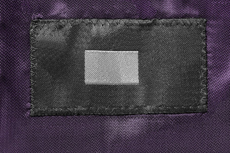 Blank textile clothes label on purple satin background closeup
