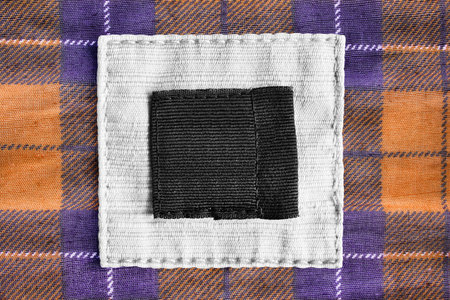 Blank black and white textile clothes label on tartan background