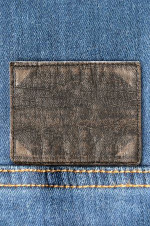 Leather patch blank clothes label on blue denim background closeup