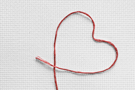 Red silk thread in the shape of a heart on white blank canvasの写真素材