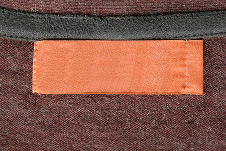 Blank textile orange clothes label on knitted brown background closeup