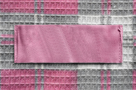 Pink blank clothes label on checkered textile background closeup
