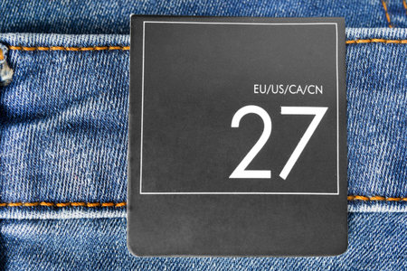 27 size clothes label on blue denim background closeup
