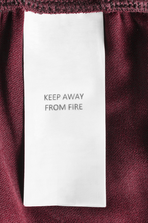 Clothes label says keep away from fire on red textile backgroundの写真素材
