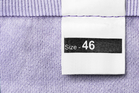 Size 46 clothes label on violet textile background closeup