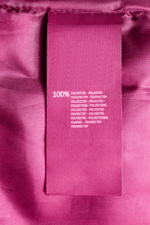 Clothes label says 100% polyester in different languages on pink textile background