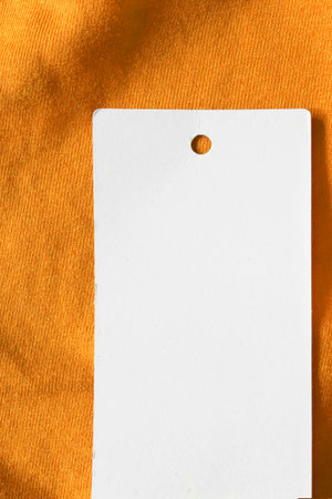 Blank paper clothes label on yellow textile background closeup
