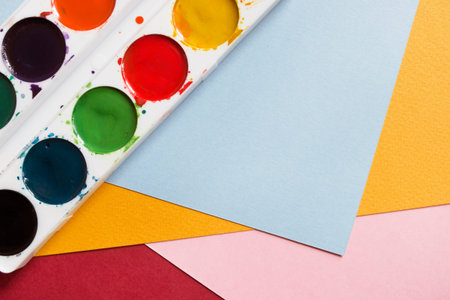 Watercolor paints on blank colorful paper sheets closeup