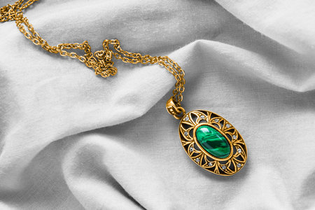 Gold necklace with vintage malachite pendant on white draped textile background