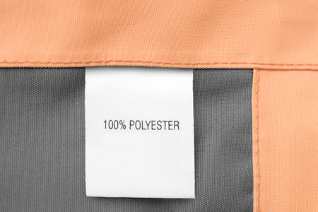 Clothes label says 100% polyester on textile background closeup