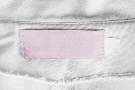 Blank pink clothes label on white textile background closeup