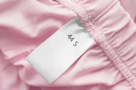 Clothing S size label on pink cotton background closeup