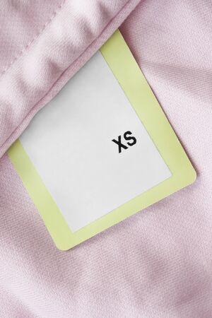 XS size clothing label on pink cotton backgroundの写真素材