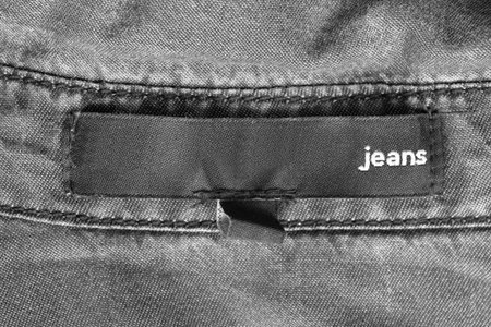 Clothing label says jeans on gray cotton background closeup