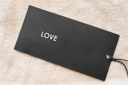Clothing label says love on beige knitted background closeup