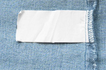 Blank clothing label on blue denim background closeup