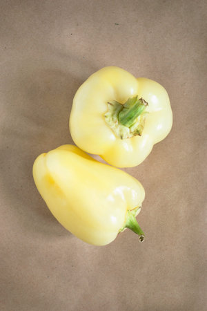 Two yellow raw bell peppers on craft paper background
