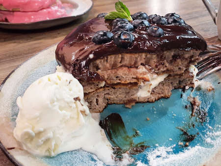 Bitten chocolate pancakes with ice cream and blueberries on blue dishの写真素材