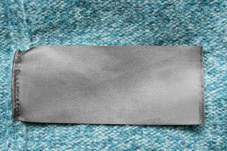 Blank textile clothing label on blue knit background closeup