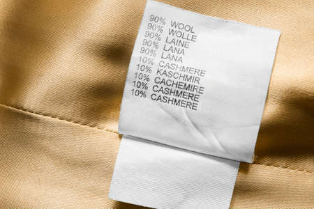 Fabric composition clothing label in different languages on golden textile backgroundの写真素材