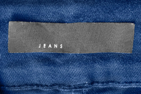 Clothing label says jeans on blue textile background closeup