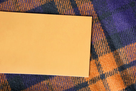 Empty yellow clothing label on tartan textile background closeup