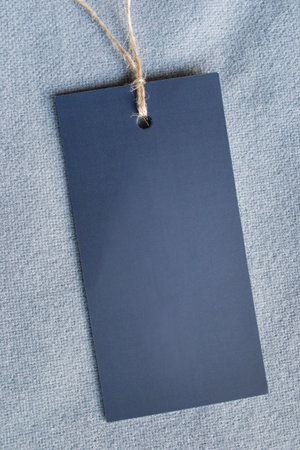 Empty paper clothing label on blue textile background closeup