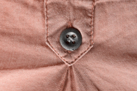 Sewn black button on brown textile background closeup