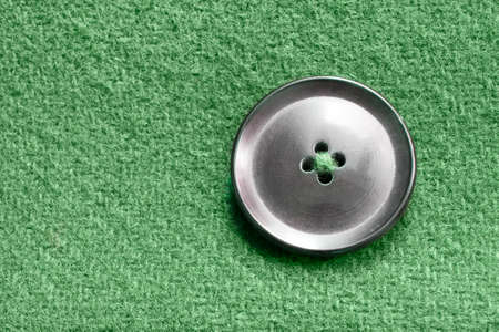 Black button sewn on green wool background closeupの写真素材