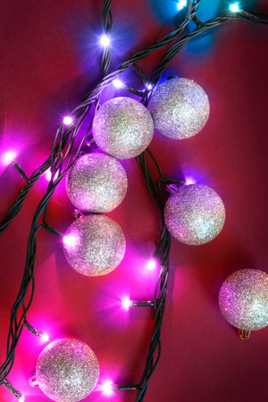 Silver christmas balls and colorful led lights on red background