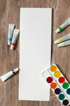 Watercolor and acrylic paints and blank sketchbook on wood backgroundの写真素材