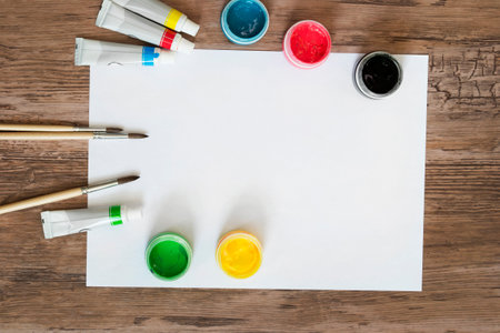 Colorful paint jars and brushes with empty white paper on wood backgroundの写真素材