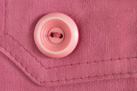 Pink plastic button sewn on pink cotton background closeupの写真素材