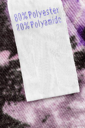 Fabric composition clothing label on violet textile background closeup