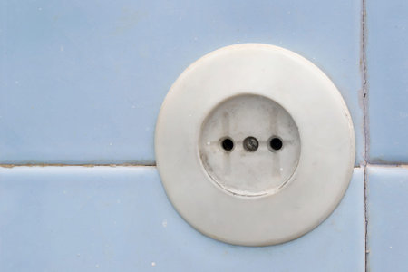 Old round european electric socket on blue tiled wall