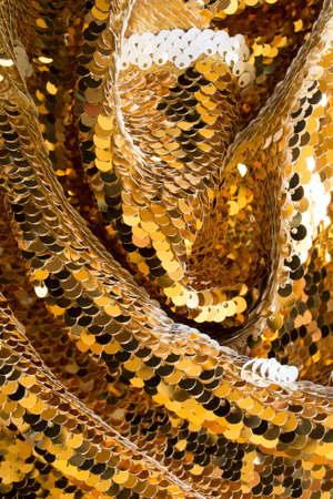 Golden shiny sequins draped fabric closeup as a backgroundの写真素材
