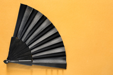 Black folding hand fan on yellow backgroundの写真素材