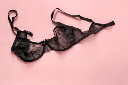Black lingerie unfastened bra on pastel pink background