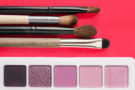 Pink eyeshadow palette and makeup brushes closeup on red backgroundの写真素材