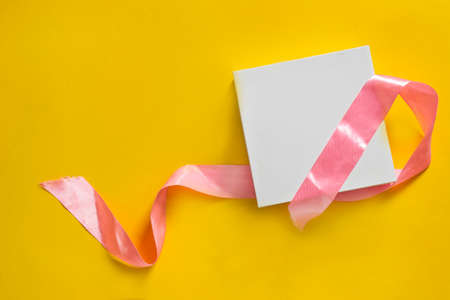White gift box with untied pink ribbon on yellow backgroundの写真素材