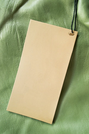 Blank craft paper clothing label on green leather background closeup