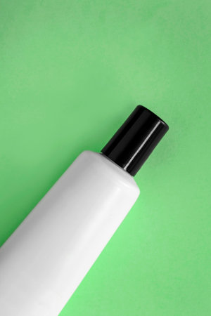 Blank white cosmetic tube on green background closeup