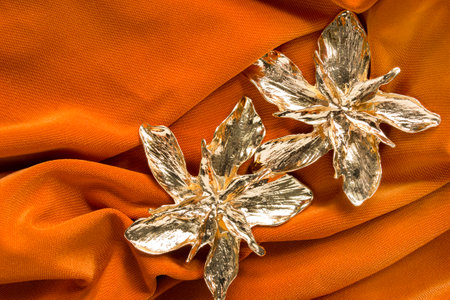 Gold large flowers earrings on orange fabric backgroundの写真素材