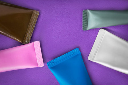 Blank plastic cosmetic tubes closeup on purple background